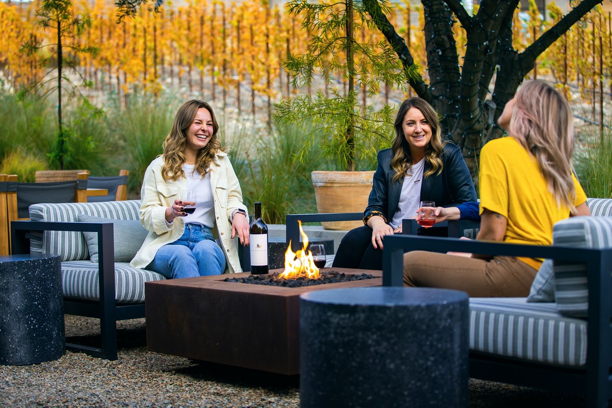 3 Woman sitting around a small firepit drinking wine